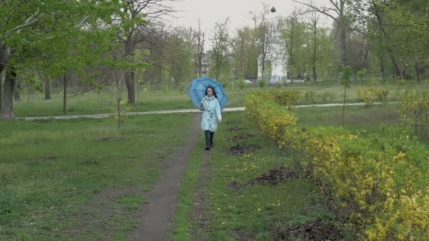Симпатичная девочка-подросток ходит с зонтиком в пустом городском парке в облачный весенний день. Ребенок с длинными волосами идет по пути к камере и оглядывается вокруг. Концепция. Портрет. 4K — стоковое видео