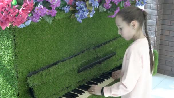 Uma adolescente feliz toca um piano verde incomum em casa, que é decorado com flores e estilizado como grama. Ideias de design. Desempenho. Close-up. 4K — Vídeo de Stock
