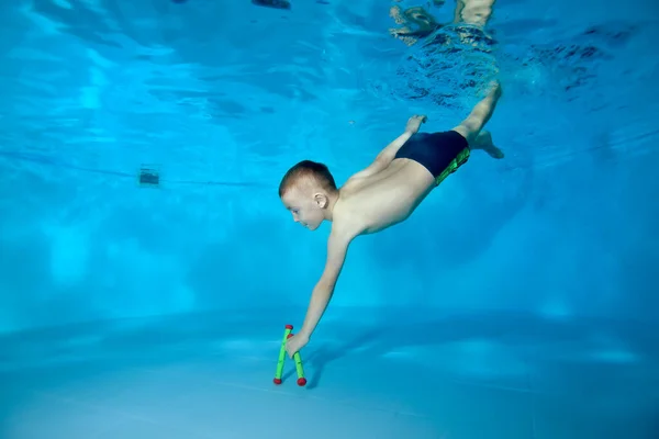 Una foto de un chico deportivo que se sumerge en el fondo de la piscina para un juguete. Buceos divertidos bajo el agua. Niño feliz activo. Clases de natación. Ejercicios corporales. Estilo de vida saludable. — Foto de Stock