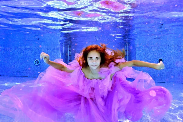 一个穿着漂亮衣服的少女的画像，她张开双臂躺在室外游泳池里，躺在水下。她的长发在水里飘扬.横向方向：. — 图库照片