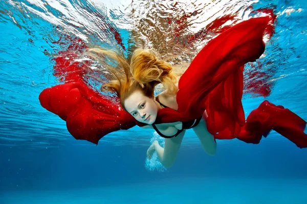 Een schattig meisje is ontspannen en heeft plezier in het buitenzwembad op een zomerse dag. Ze duikt onder water en zwemt met een rode doek in haar handen terwijl haar haar vliegt. Portret. Onderwaterfotografie. — Stockfoto