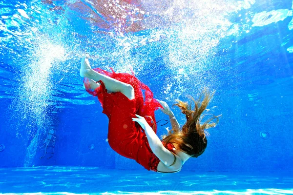 Una chica se ahoga y se hunde en el fondo de la piscina con la espalda hacia abajo, rodeada de burbujas de aire en un vestido rojo en un día de verano brillante. Su cara está cubierta por su pelo. Concepto. Sin rostro. — Foto de Stock