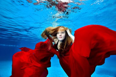 Yüzen ve elinde kırmızı bir bezle havuzda oynayan uzun saçlı tatlı bir kızın portresi. Moda portresi. Su altı fotoğrafçılığı. Yatay yönelim.