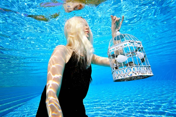 Retrato surrealista de una chica rubia bajo el agua en una piscina al aire libre. Ella posa con un vestido negro y tiene un cheque blanco. Su cara está cubierta por su pelo. Sin rostro. Colores brillantes. Fotografía moda. —  Fotos de Stock