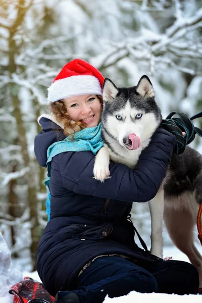 Una joven en un bosque de invierno con un perro Husky. La chica sonríe y mira a la cámara. Orientación vertical. — Foto de Stock