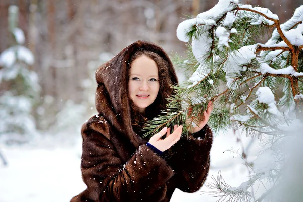 공원의 어느 화창 한 겨울날 모피 코트를 입은 어린 소녀의 모습. 그 소녀는 카메라 를 부드럽게 바라본다. 전나무의 가지들이 눈 속에 있지. 수평 방향. — 스톡 사진