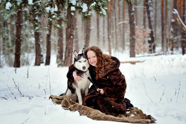 Imagen de una hermosa chica con un perro Husky en un parque de invierno. Se acurrucó con el perro. Una chica con un hermoso abrigo de piel. Un hombre sobre nieve blanca con un perro. Personas y perros. — Foto de Stock
