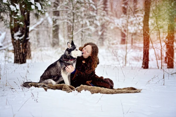 Marco con una hermosa chica y un perro Husky en un parque de invierno. Ella mira al perro tiernamente. Un hombre sobre nieve blanca con un perro. Personas y perros. Orientación horizontal. — Foto de Stock