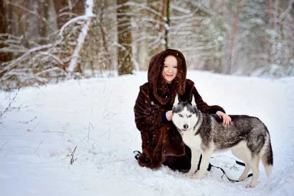 Un paseo en un día soleado con un perro Husky en un parque de invierno. La chica abraza suavemente al perro por la cruz y mira a la cámara. Un hombre sobre nieve blanca con un perro. Personas y perros. Ternura. Amistad. — Foto de Stock