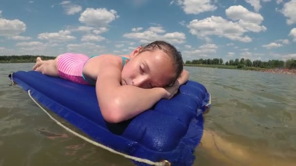 A tanned little girl swims and rests on an air mattress in the middle of a lake far from the beach. She has closed her eyes and is sleeping on a bright sunny day. The concept. Close-up. 4K — Stock Video