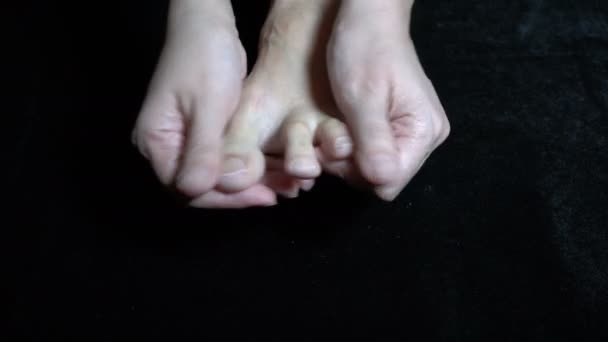 La mujer masajea y amasa su pie descalzo con sus manos, que está apretado, y sus dedos en ella. Disparando sobre un fondo negro. Plan detallado. Vista superior. Concepto. 4K — Vídeos de Stock