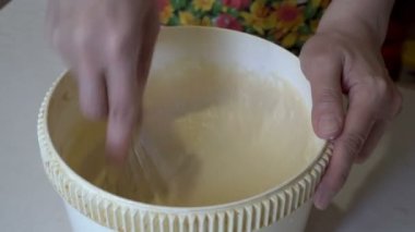 Yetişkin bir kadın ev mutfağında beyaz bir kâse içinde hamuru çabucak hazırlar. Tatlı bir tatlıyı hazırlıyorum. Çalışırken kadınların ellerinin yakın plan çekimleri. Üst Manzara. Yüzsüz. 4K