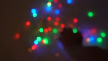 Alışılmadık Noel ışıkları. Yakın plan, bulanık erkek elleri siyah arka planda çok renkli yanıp sönen ışıkları karıştırıyor. Siluet. Arka plan bulanık. 4K