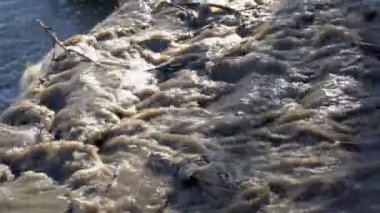 Enkaz, dallar ve plastikten oluşan kirli, kahverengi bir su akıntısı nehre akıyor. Çevre kirliliği kavramı. Yakın plan. 4K