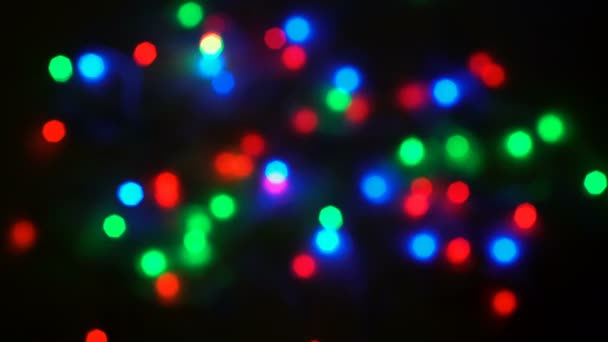 Coloridas luces borrosas de la guirnalda brillan en un ritmo diferente sobre un fondo negro. Iluminación navideña. Hermoso bokeh. Primer plano. 4K — Vídeos de Stock