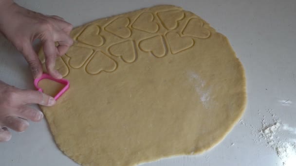 Bir kadın kurabiye hazırlar ve çiğ hamurdan kalp şeklinde kuru boşluklar çıkarır. Ev mutfağında yemek pişirmek. Kadınların ellerinin yakın çekimi. Yüzsüz. Üst Manzara. 4K — Stok video