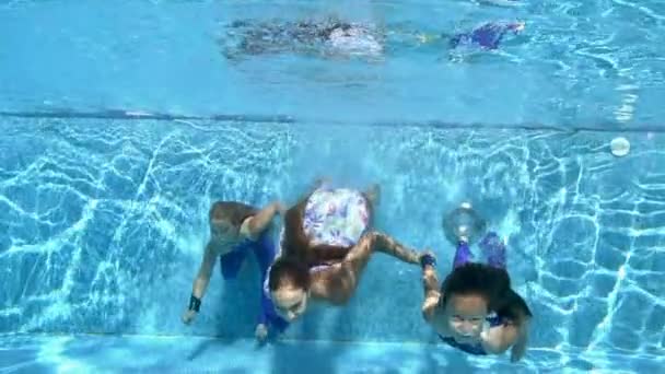 在一个阳光灿烂的夏日，三个可爱的小女孩手牵手在室外游泳池里游泳。他们看着相机笑了。快乐假期的概念。慢动作4K — 图库视频影像