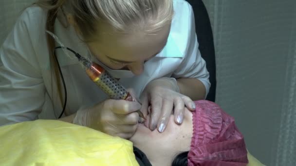 Una cosmetóloga femenina hace un procedimiento permanente de maquillaje labial para una joven en un salón de belleza. El trabajo de un cosmetólogo. Primer plano. 4K — Vídeo de stock