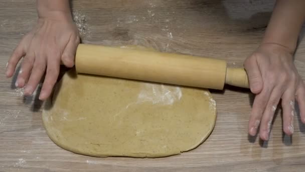 Женщина катит желтое сырое тесто в тонкий блин деревянной скалкой на домашней кухне. Крупный план. Вид сверху. 4K — стоковое видео