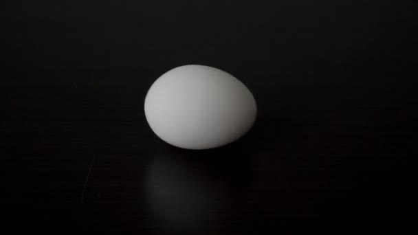 Un huevo de gallina blanco y crudo gira por sí solo sobre una mesa negra. Realismo conceptual. Primer plano. Copiar espacio. 4K. — Vídeos de Stock