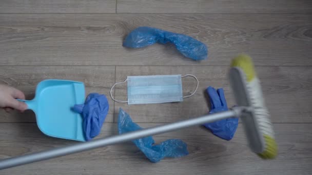 Covid-19 waste. The cleaner sweeps away the used disposable personal protective equipment, face masks and gloves with a broom. The concept of environmental protection. Close-up. Top view. Faceless. — Stock Video