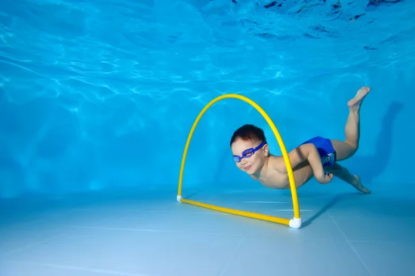 Un bambino felice nuota sott'acqua nella piscina dei bambini. Fa sport e nuota attraverso un cerchio in fondo alla piscina. Ritratto. Concetto. Orientamento orizzontale della foto. — Foto Stock