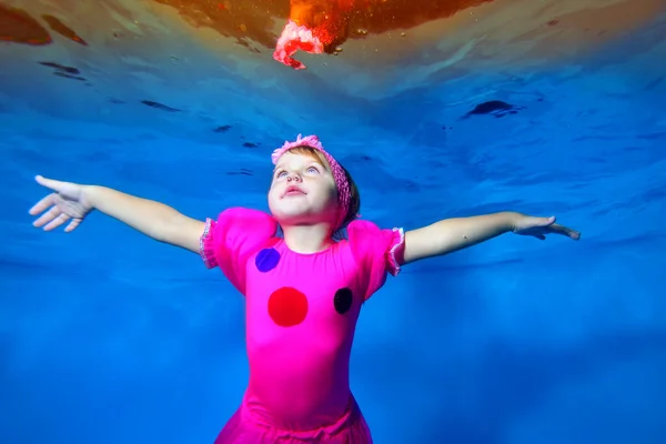 Şirin küçük kız havuzda yüzüyor ve poz veriyor kırmızı bir elbiseyle, kolları yana doğru açık. Portre. Yatay görünüm. — Stok fotoğraf