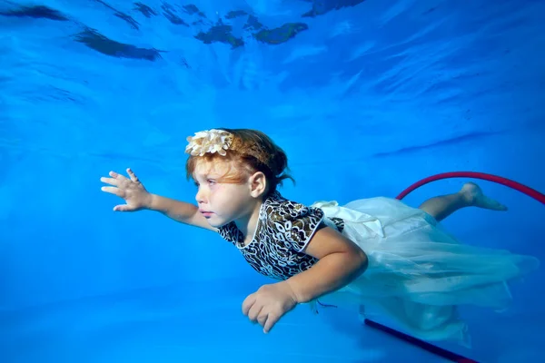 Una hermosa niña está nadando bajo el agua en la piscina en un hermoso vestido blanco, cerca de la parte inferior. Retrato. Vista horizontal. — Foto de Stock