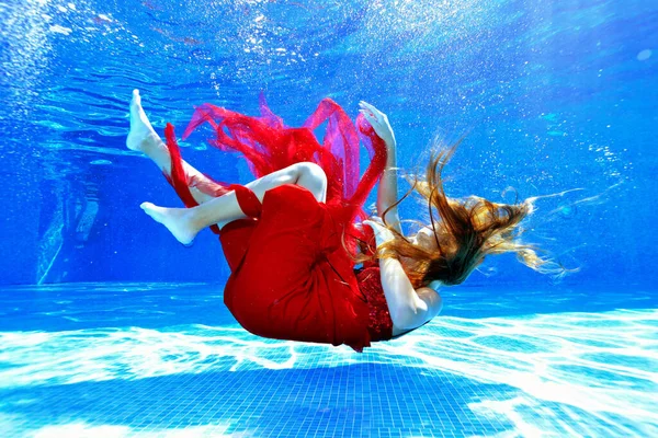 Uma jovem se afoga e afunda no fundo da piscina em um vestido vermelho. O cabelo comprido cobre-lhe o rosto. Conceito. Orientação horizontal. — Fotografia de Stock