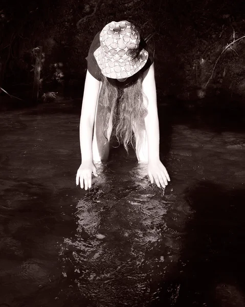 Ragazza in piedi nel fiume piegandosi in avanti e immergendo le mani in — Foto Stock
