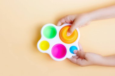 Elinde oyun tutan bir çocuk. Stres önleyici duyusal oyuncaklar. Pastel arka planda basit gamzeler. 
