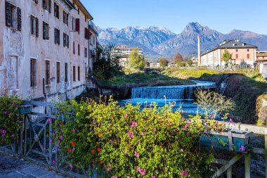 Huzurlu nehir, dağlarla ve binalarla çevrili Belluno, Veneto, İtalya 'nın tarihi merkezi Feltre' deki yeşil arazide akar ve barışçıl bir atmosfer yaratır ve doğanın güzelliğini ön plana çıkarır.