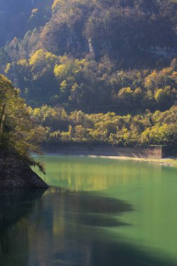 Tranquil river flows through a picturesque landscape, reflecting colorful autumn leaves and surrounded by verdant hills and rocky formations, showcasing natures beauty