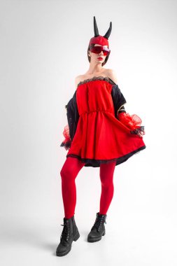 Kırmızı taytlı ve siyah çizmeli seksi şeytan kız beyaz stüdyo arka planında poz veriyor..