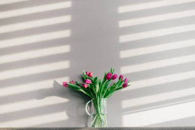 Gri duvarda bir buket güzel lale olan cam vazo.