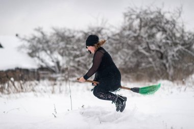 Karlı bir kış günü kırsal kesimde, süpürge sapında kılık değiştiren kostümlü heyecanlı kız..