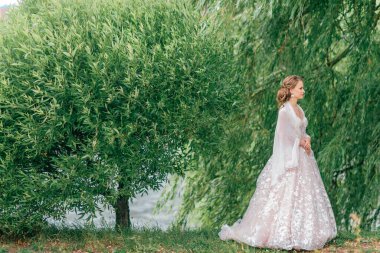 Beyaz gelinlik içinde güzel bir gelin elinde çiçeklerle dışarıda poz veriyor..