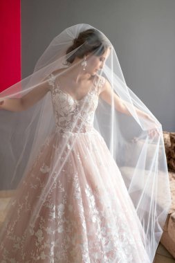 Gri arka planda, elinde çiçekle poz veren beyaz elbiseli güzel gelinin portresi.