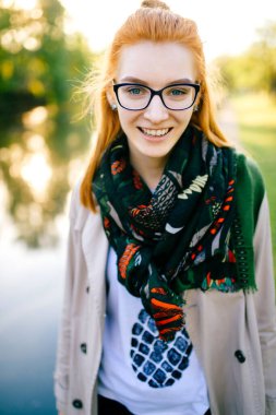 Açık renk paltolu ve boynunda eşarpla büyüleyici kızıl saçlı genç bir kadın güneşli bir günde doğada duruyor. Sonbaharda göl kenarında şık genç elbiseli ince bir bayan yürüyor. Park 'ta yürü