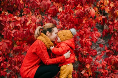 Beyaz ceketli, siyah pantolonlu, gri spor ayakkabılı yakışıklı anne sıcak, parlak elbiseli küçük oğluyla sarılıp seviniyor..