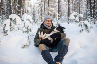 Karlı ormanda sevimli köpeği elinde tutan mutlu bir adam. Kış ormanında sevimli köpek yavrusuna sarılan gülümseyen çocuk. Hayvan sever. Köpek - insanın arkadaş konsepti.