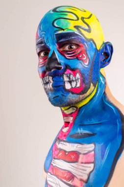 Kafasında ve omzunda kırmızı-sarı eldivenler, siyah pantolon ve botlarla, tişörtsüz, tuhaf bir adamın portresi.