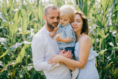 Açık mavi elbiseli genç, beyaz gömlekli, kısa siyah saçlı, beyaz pantolonlu, güçlü beyaz saçlı, yaz aylarında mısır tarlasında sarışın oğluyla oynayan güzel bir anne..