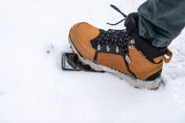 Kahverengi çizmeli erkek bacağı karda uzanan akıllı telefona basıyor. Telefon koruyucu cam kavramı.