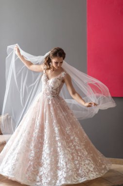 Gri arka planda, elinde çiçekle poz veren beyaz elbiseli güzel gelinin portresi.