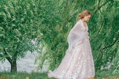 Beyaz gelinlik içinde güzel bir gelin elinde çiçeklerle dışarıda poz veriyor..