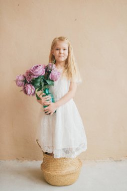 Sarı arka planda saman sepetinde duran beyaz elbiseli güzel, uzun saçlı kız çocuğu. Elinde bir buket çiçekle elinde vazo tutan güzel bir kadının ev yapımı portresi.