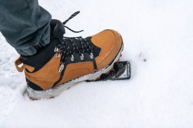 Kahverengi çizmeli erkek bacağı karda uzanan akıllı telefona basıyor. Telefon koruyucu cam kavramı.