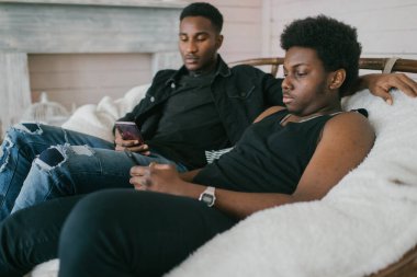 İki mutlu yetişkin Afrikalı erkek, dekoratif stüdyo sahasında birlikte oturup rahatlıyor. İki Afro-Amerikan erkek kapalı mekan yaşam tarzı vintage tarzı portre