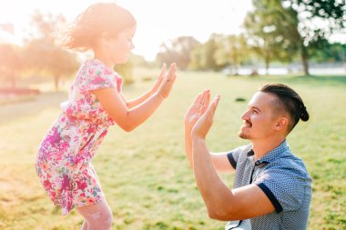 Baba ve kızı yaz açık hava aktiviteleri. Sevgi dolu baba, sevimli bebeğine tapar. Ebeveyn ve çocuk parkta eğleniyor. Tasasız çocukluk. Mutlu aile portresi. Neşeli kız alkışlıyor.